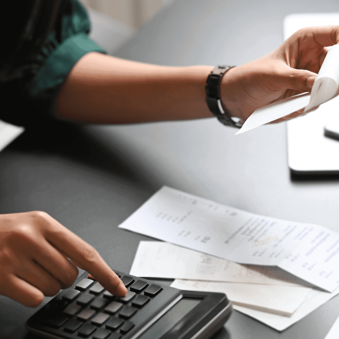 A person using a calculator and reviewing financial documents on a desk.