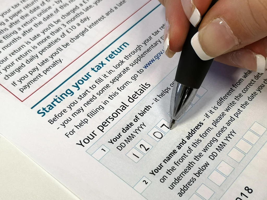 Close-up of a hand holding a pen over a tax return form, preparing to fill in personal details.
